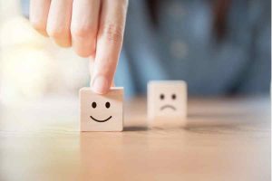 Two cubes - one with sad face and another with a smiling face. A man chooses the happy face.