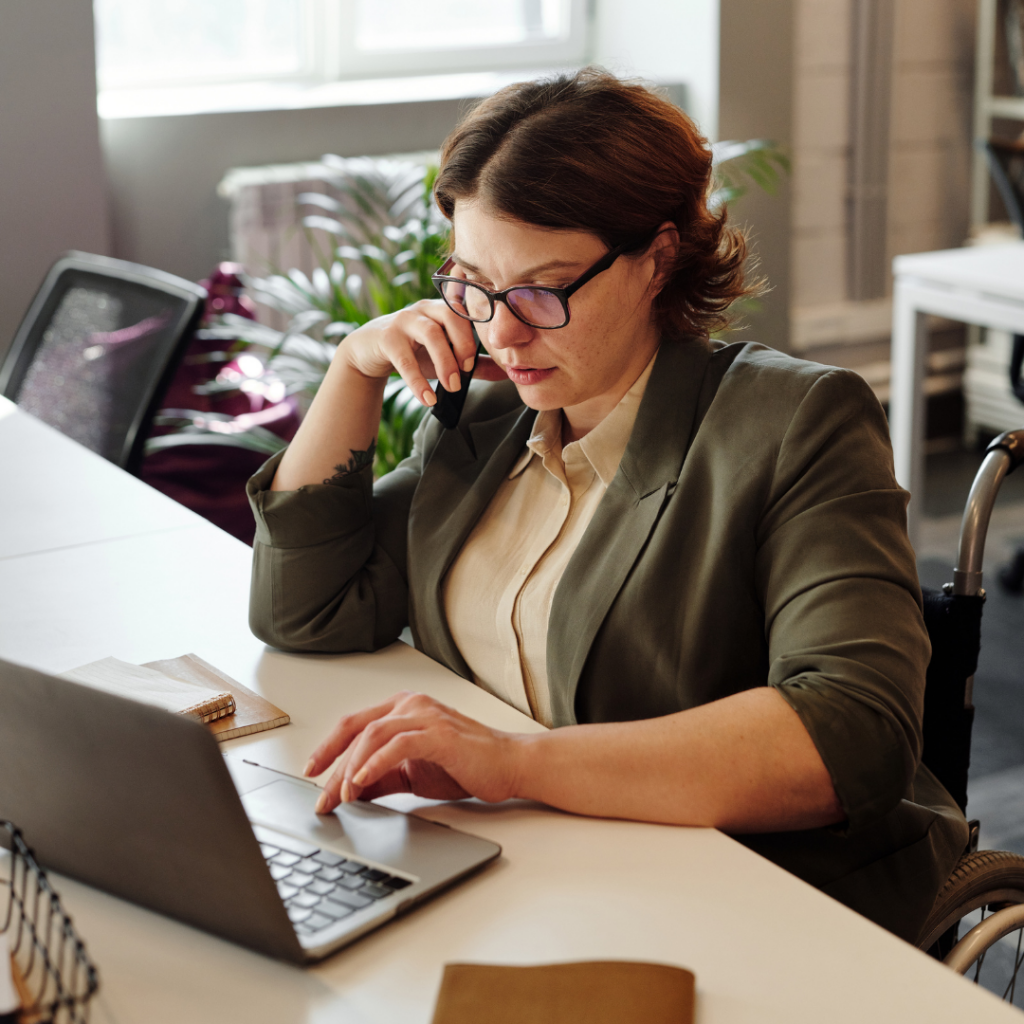 A woman sitting and answering a phone while working on a computer.