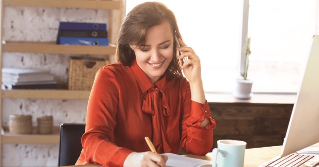 woman smiling on phone writing down a message