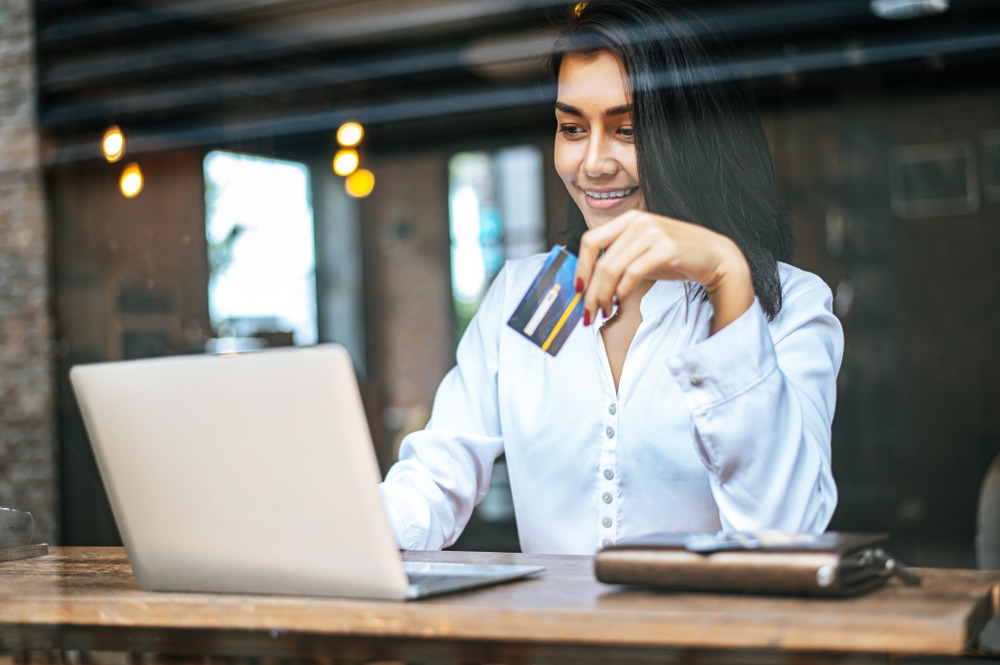 Woman sat with a laptop and paid with a credit card in a coffee shop.