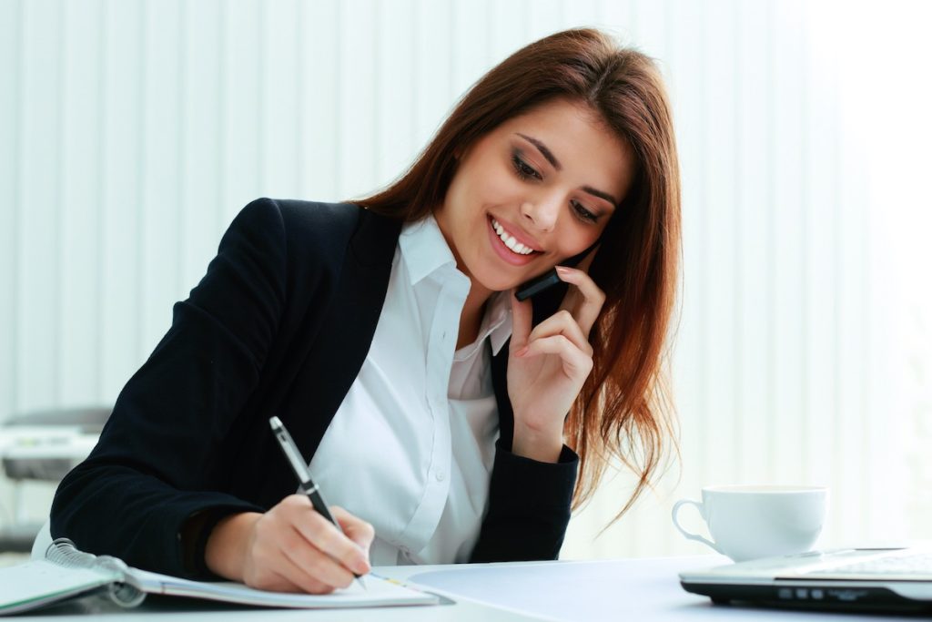 Smiling female receptionist taking notes for call centre service