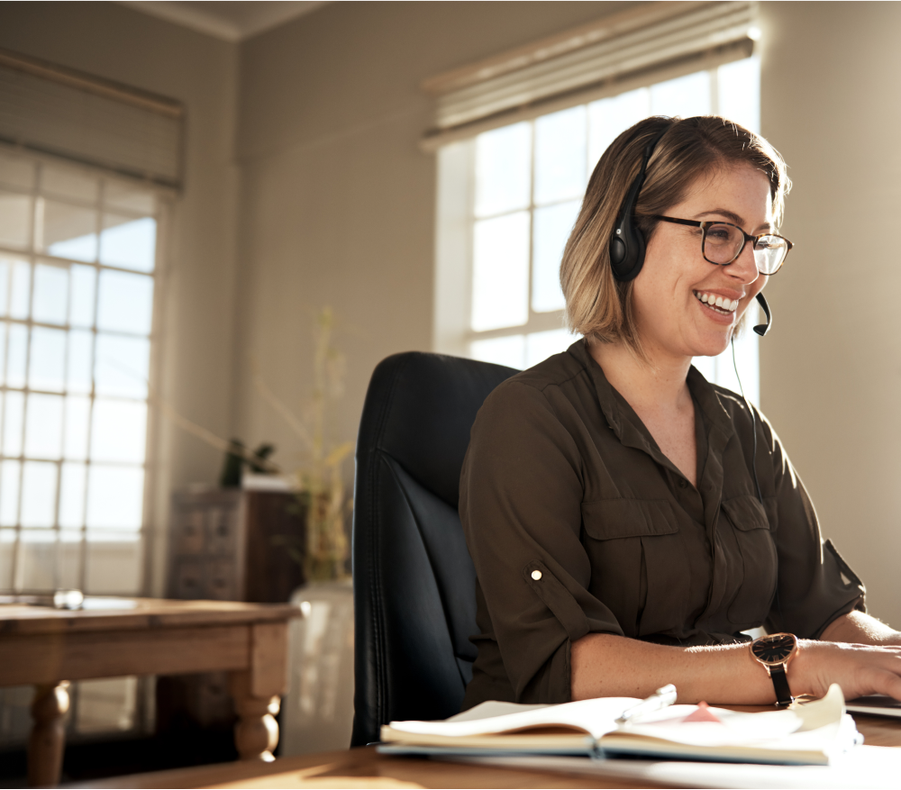 Smiling receptionist in home setting taking call with customer via headset