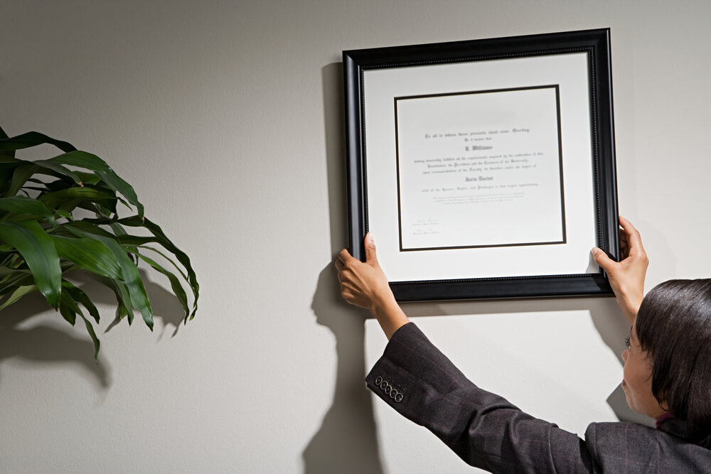 Businesswoman putting up framed credentials in office