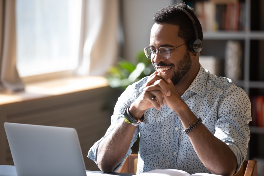 Man on phone sat in front of laptop happily 

