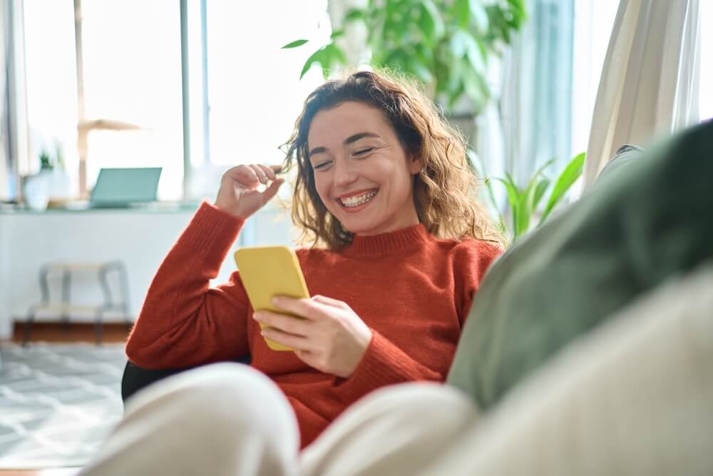 Smiling woman sat on sofa happy with customer interaction on smartphone

