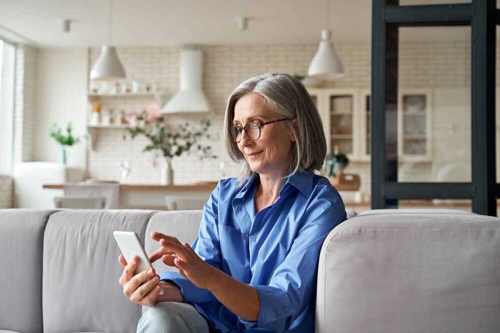 Smiling woman sat at home typing on smartphone engaged in customer interaction