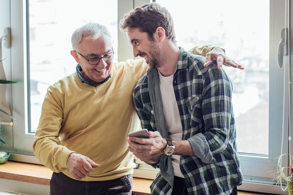 Happy older and younger man bonding over a smartphone, smiling and sharing a moment indoors