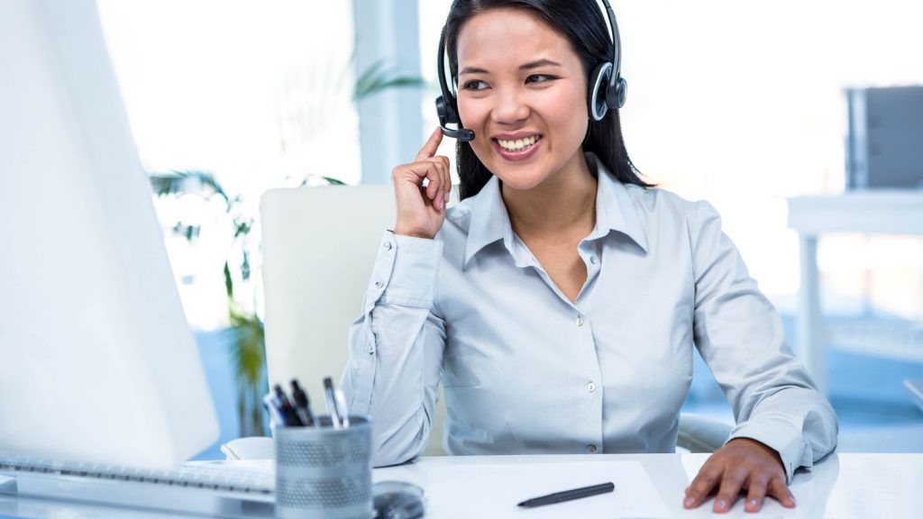 Smiling answering agent in white room setting online appointment for caller