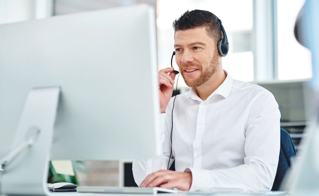 Man on a headset, sitting in front of a laptop, answering calls as part of a telephone answering service.