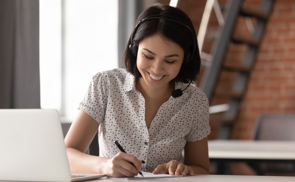 Woman, wearing a headset, taking notes from a customer who has called a telephone answering service.