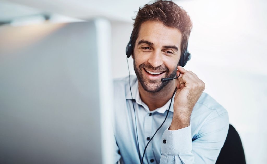 Smiling man answering calls using a headset as part of a telephone answering service job.