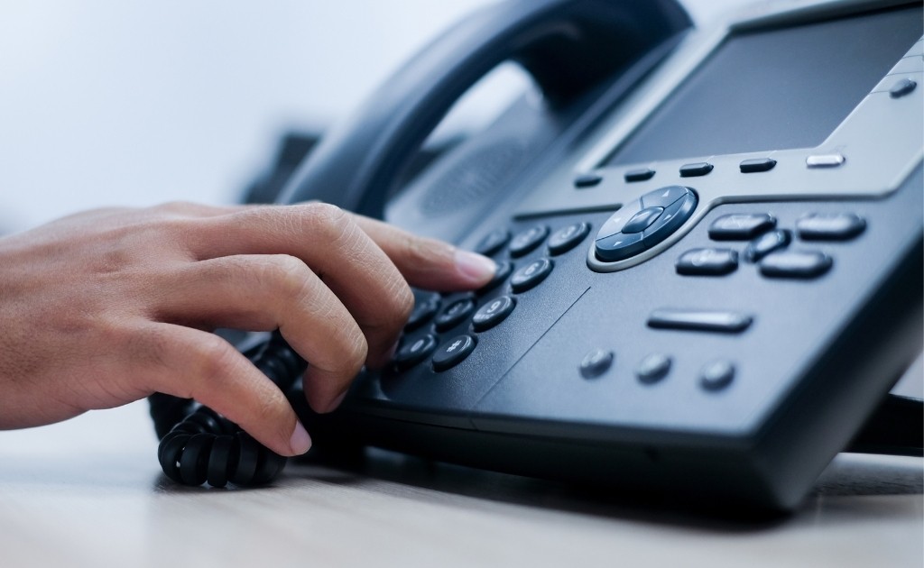 Hand dialing a button on an office phone to make a business call.
