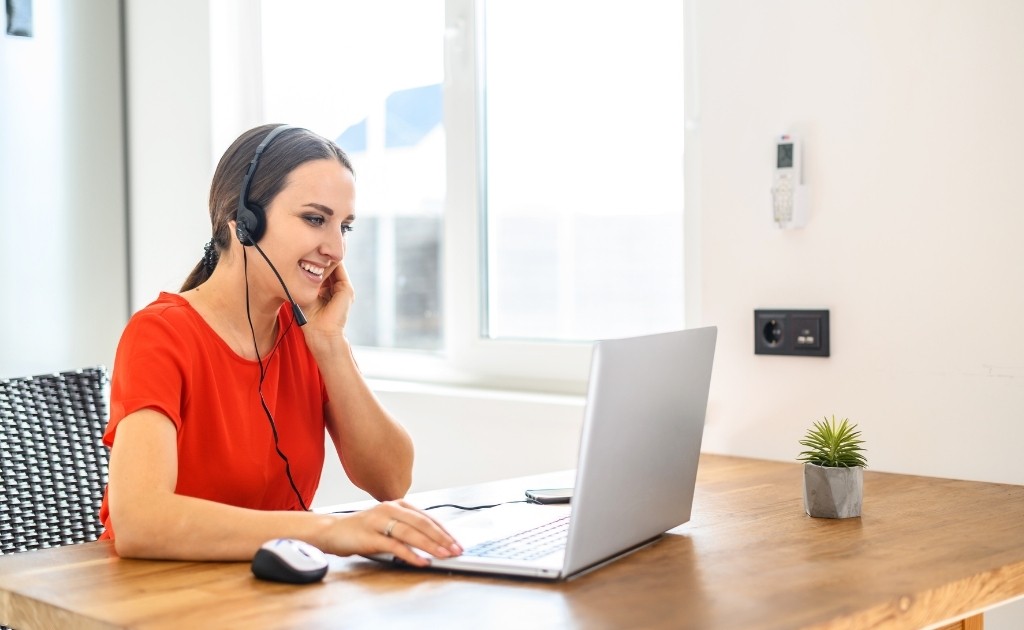 A smiling woman, working at a desk wearing a headset to answer calls as part of her call handling job.