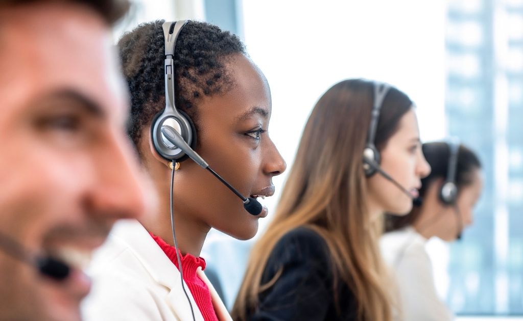 Four people, answering calls using headsets as part of their job at an inbound call centre.