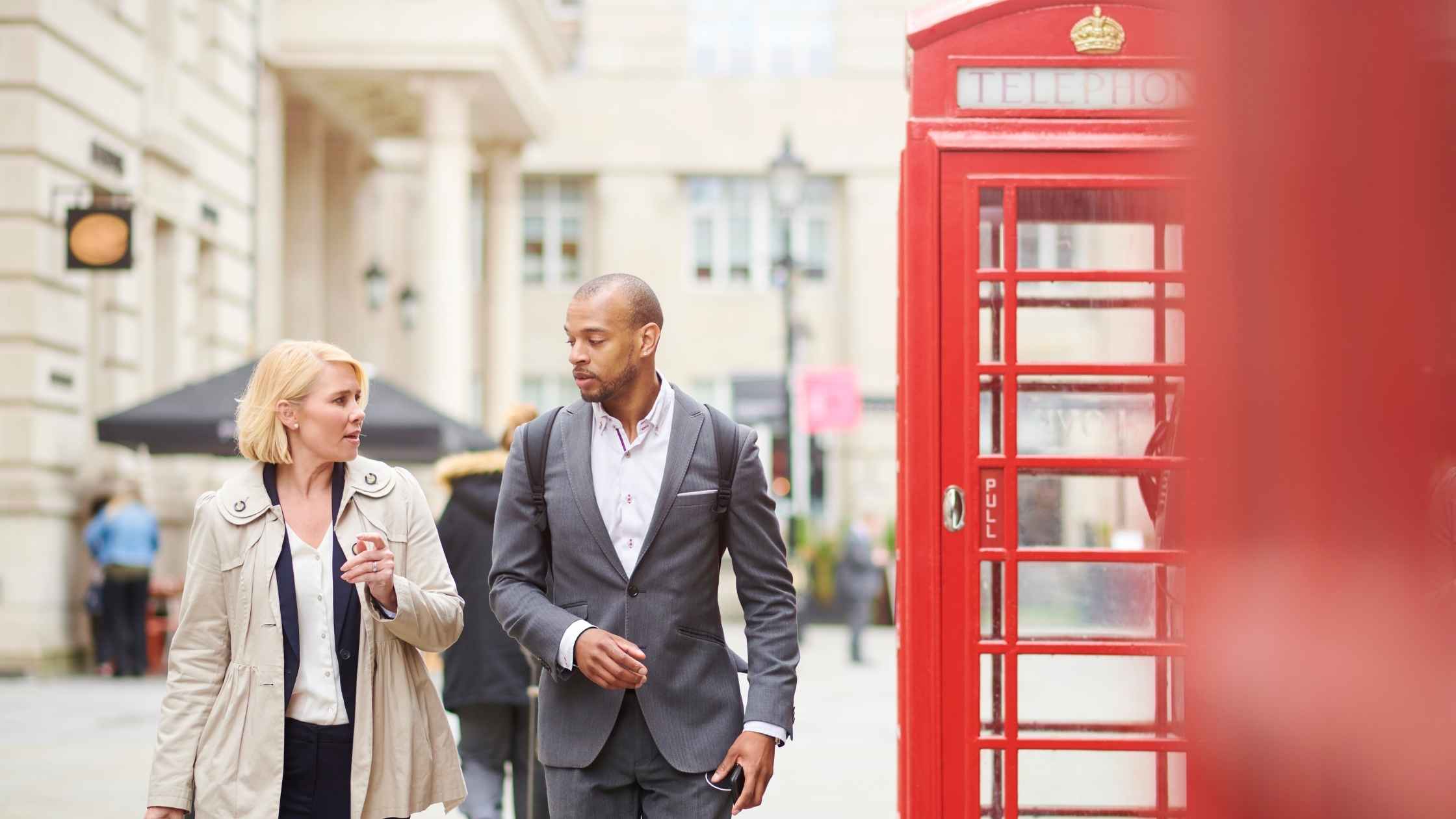 Smiling man and woman walking past a red UK public telephone box
