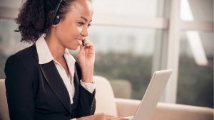 Smiling woman working as a virtual assistant, chatting to a customer on a headset, sitting in front of a laptop.