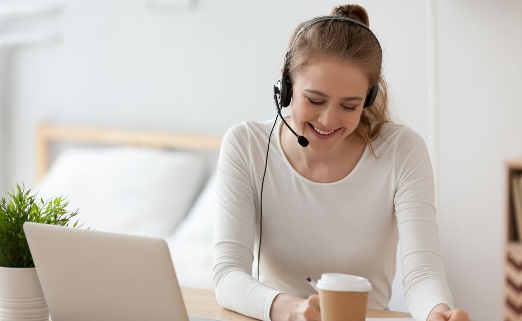 Woman answering calls as a virtual assistant using a headset, sitting at a desk with a cup of coffee.