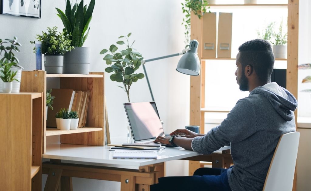 Man participating in remote work at a desk with his laptop, surrounded by plants.