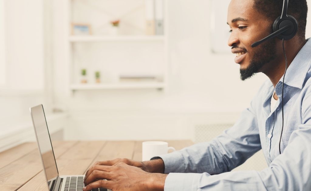 Man working as a UK virtual receptionist, answering calls on a headset, typing on a laptop.