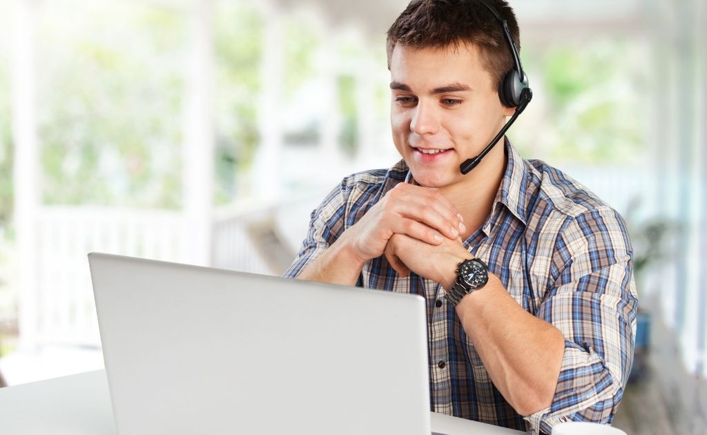 Smiling virtual receptionist, working from home, answering calls using a headset in front of a laptop.