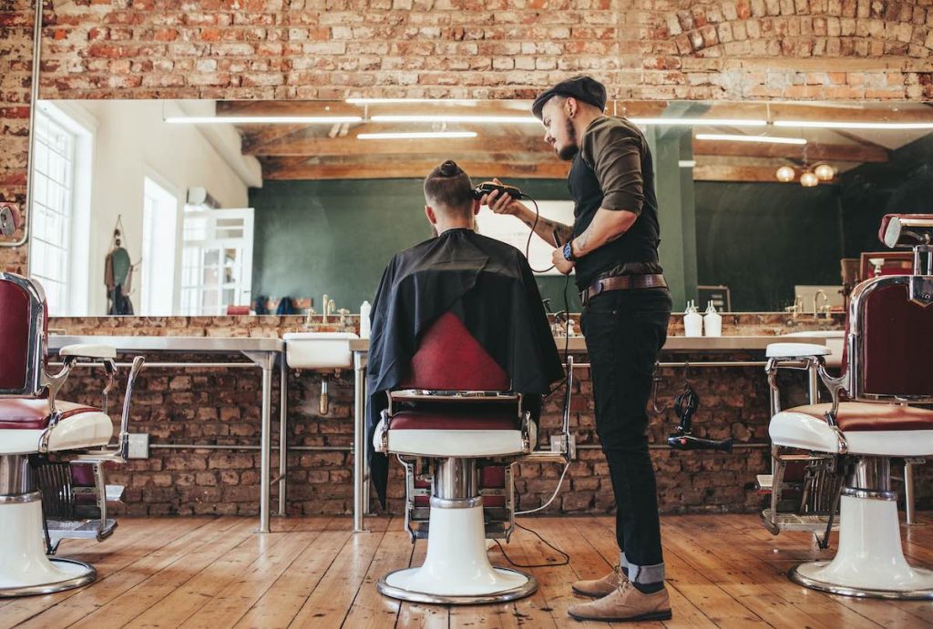 Man cutting customers hair in barbers booked in using appointment scheduling