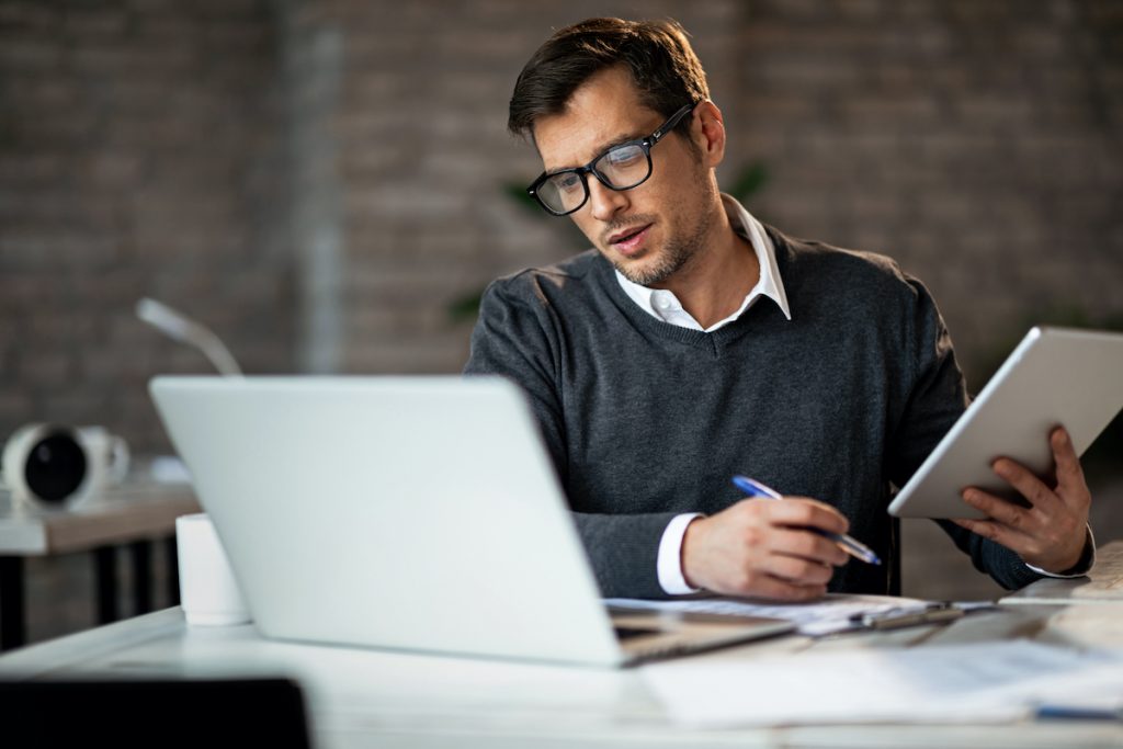 Man taking notes during video meeting looking to drive down small business costs