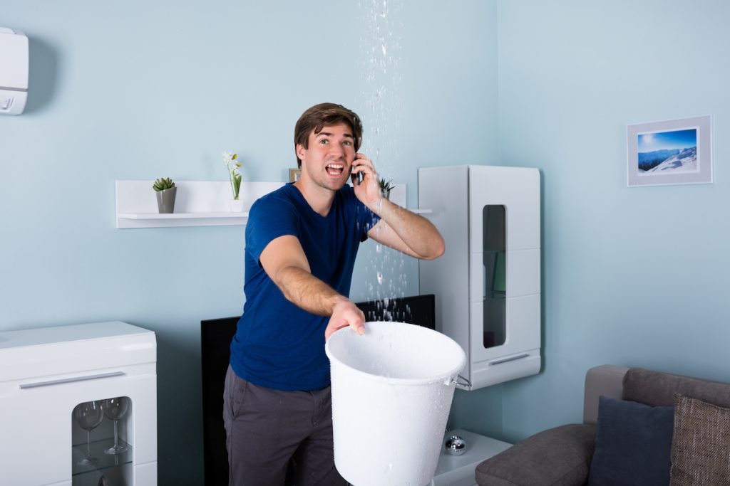 Worried Man Calling facilities management service While Leakage Water Falling Into Bucket At Home