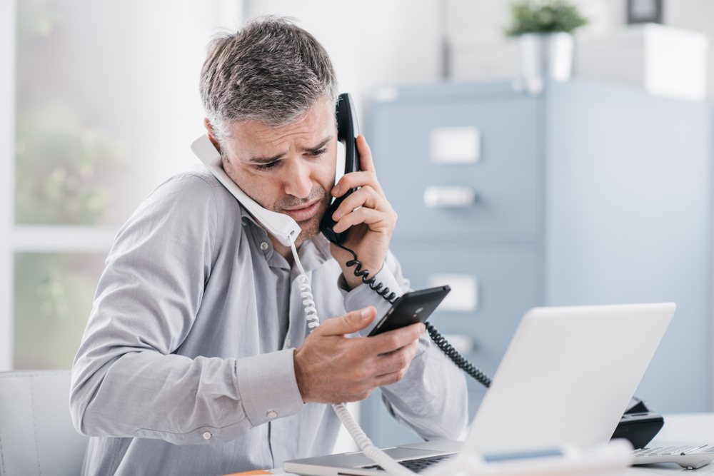 Stressed businessman in office trying to answer multiple calls o different devices