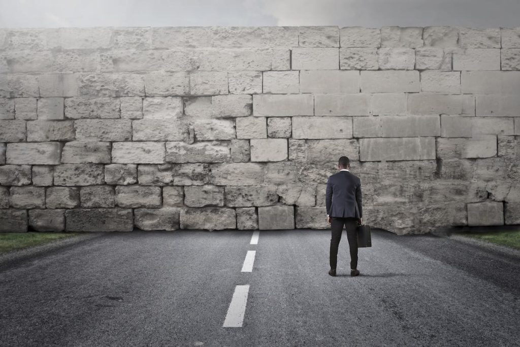 Businessman facing a big stone wall to represent qualifying questions challenge