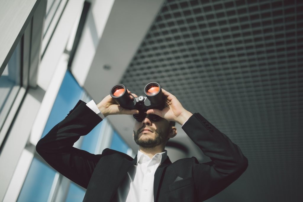 Businessman with binoculars spying on competitors resenting probing qualifying questions