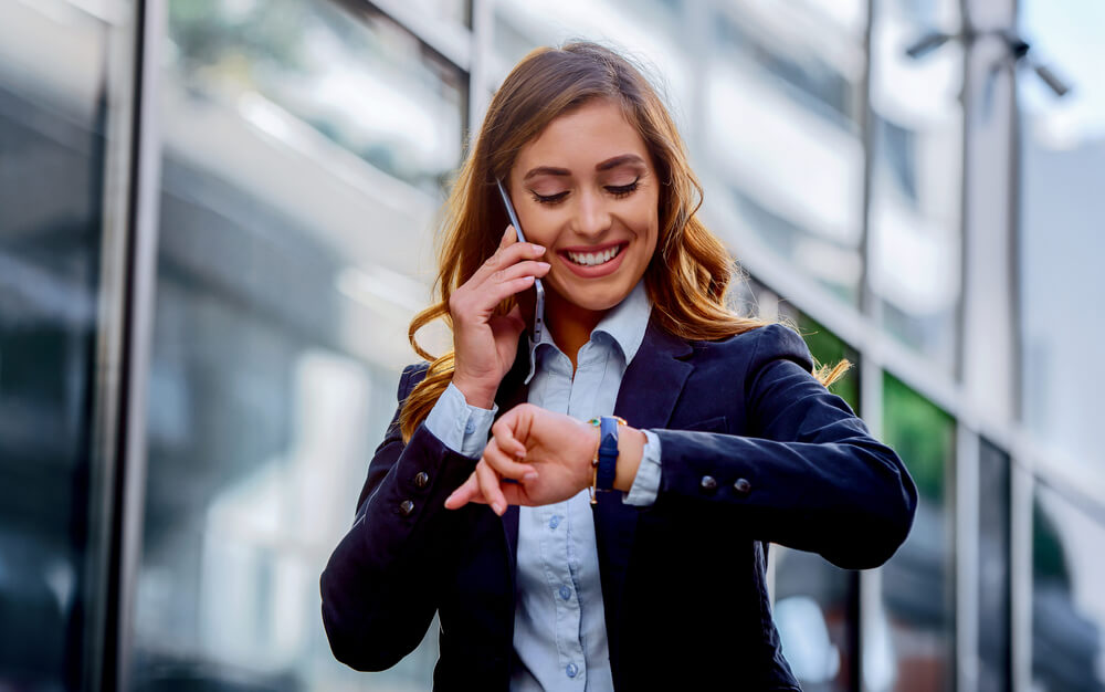 Smilig businesswoman looking at her watch while on the phone