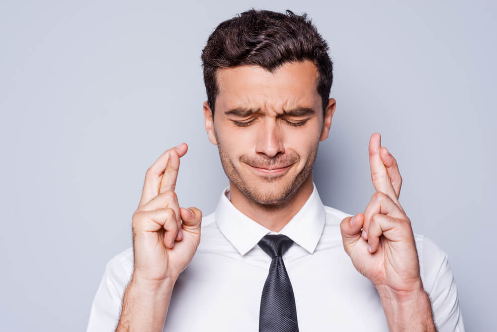 Man in shirt and tie with eyes closed and fingers crossed