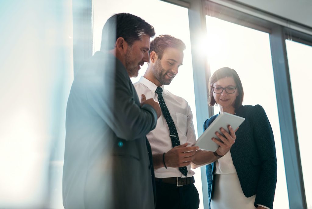 Colleagues standing looking at a tablet in front of office window