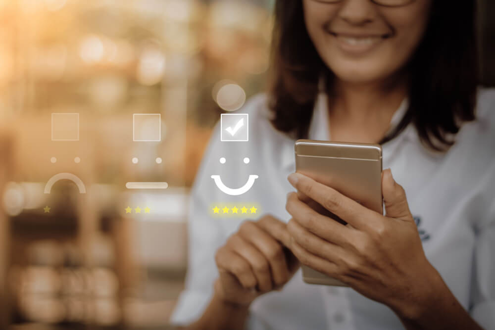 Visual showing a woman checking a smiling face box visual on smartphone representing a satisfied customer