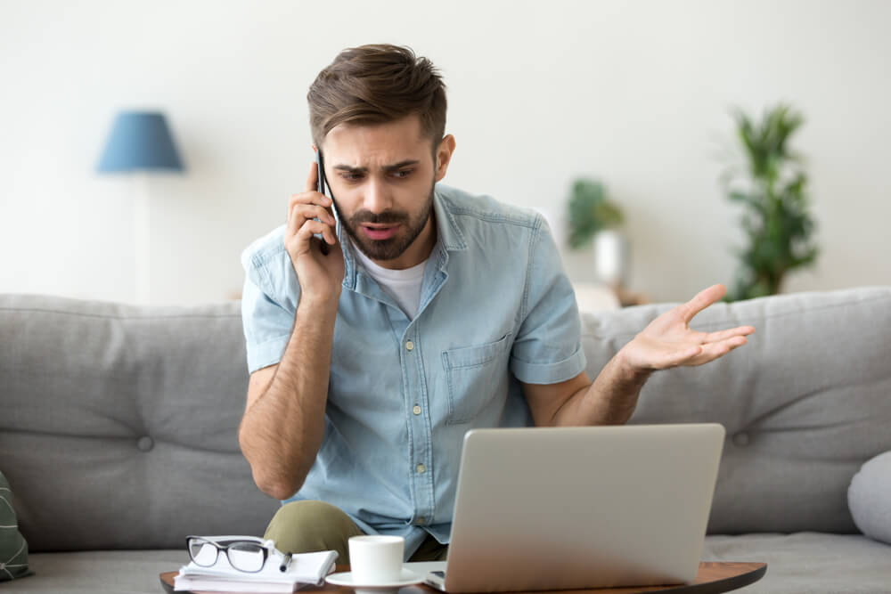 Angry man talking on phone with laptop on table in front of him