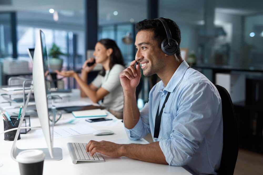 Smiling virtual receptionist at computer with headset in office setting