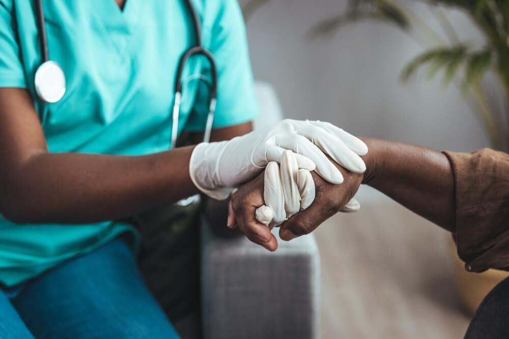 The nurse comforts the elderly individual by holding their hand.