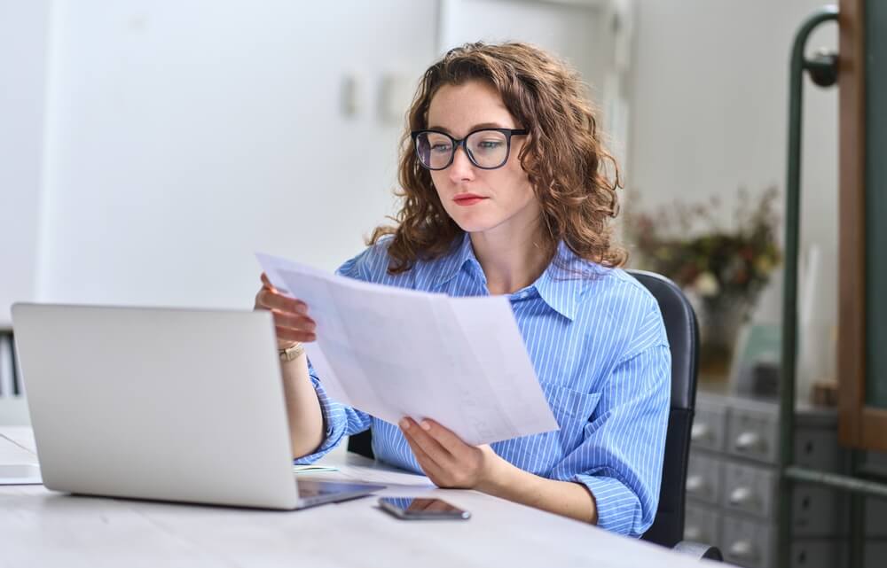 A woman sitting at a desk looking at a piece of paper in her office.