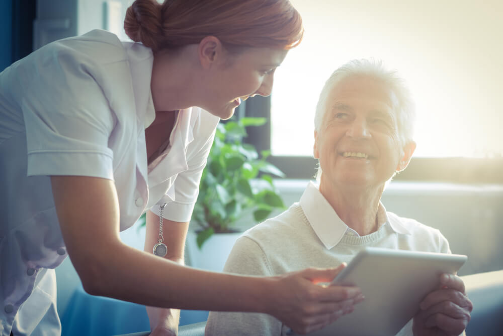 A nurse assists an elderly man with a tablet.