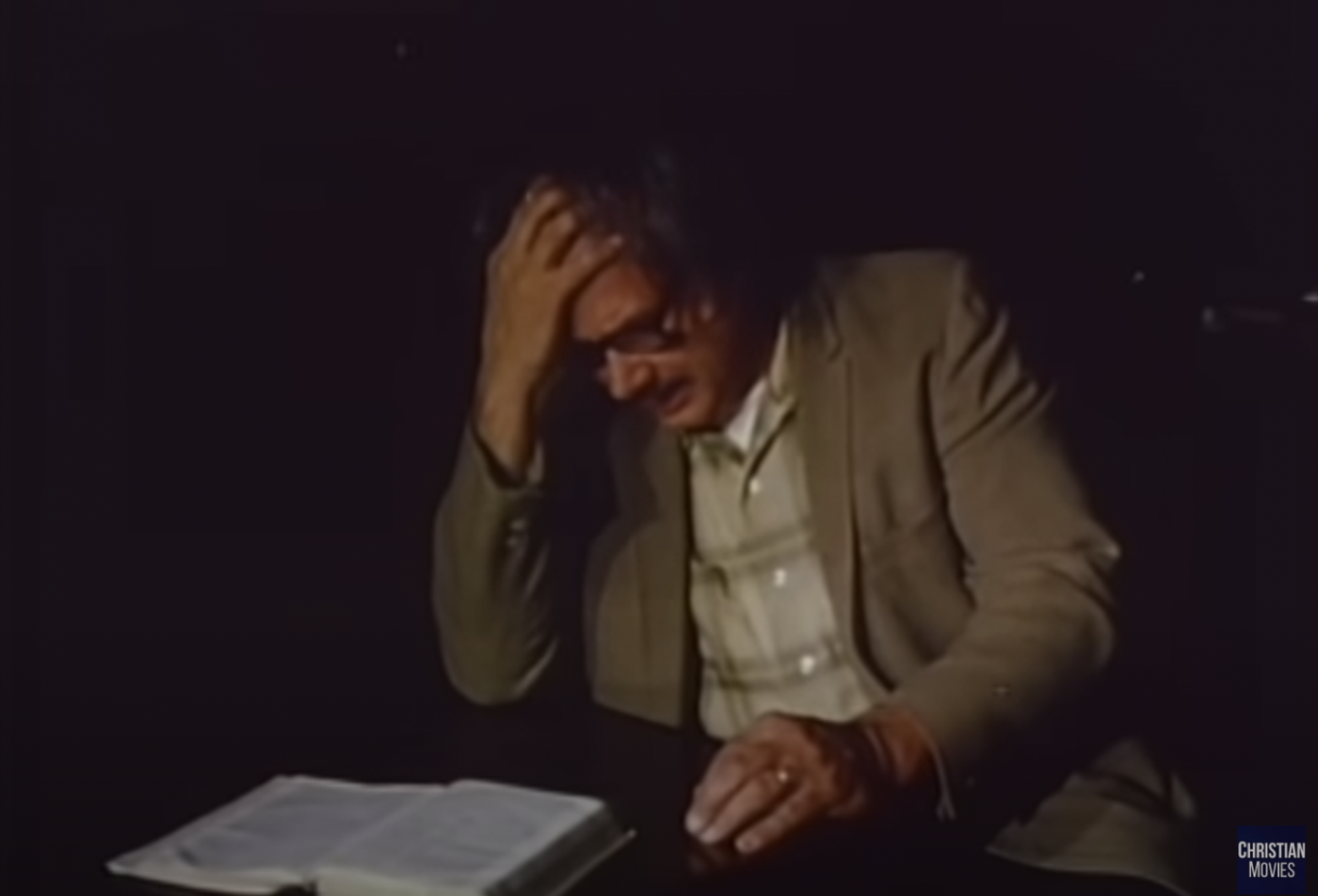 Reverend Turner putting his right hand up to his brow while reading the Bible in the dark.