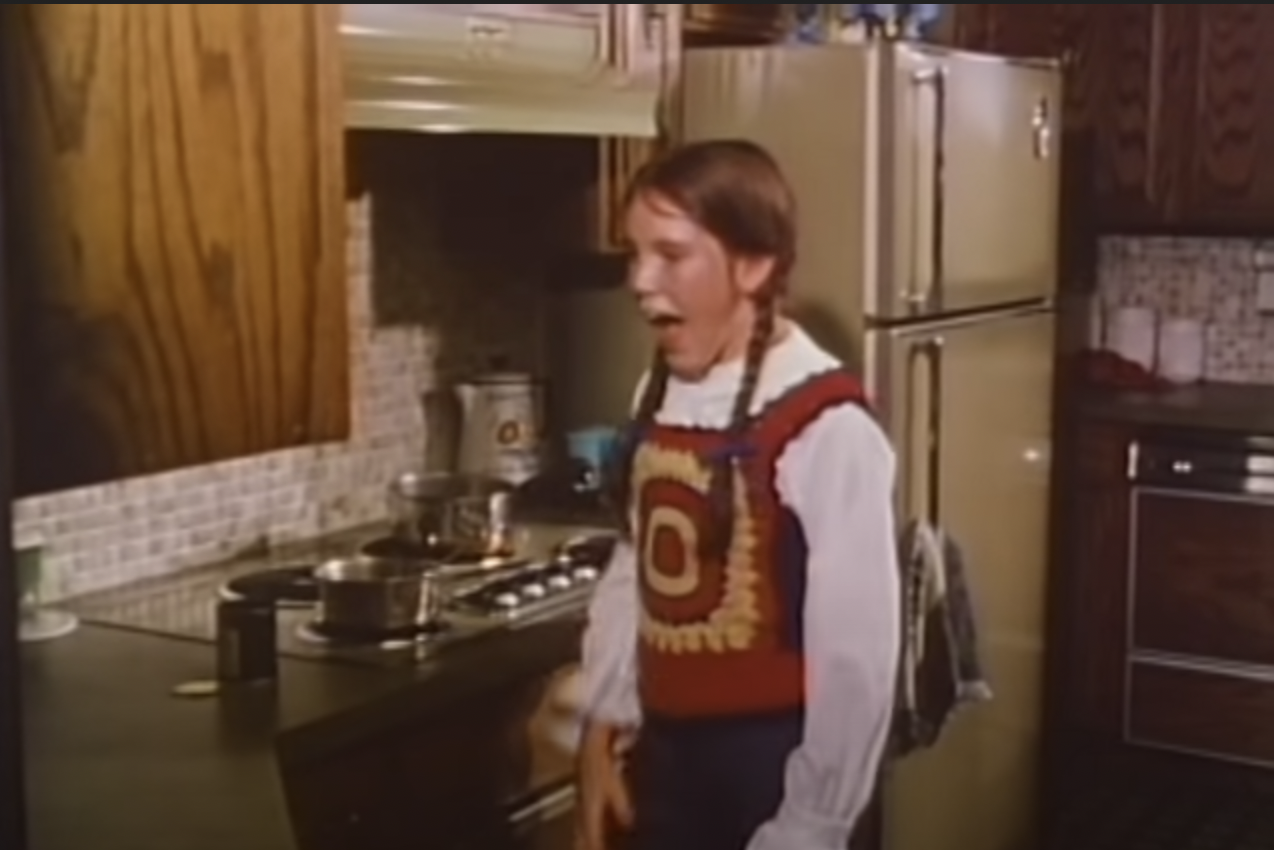 A pre-teen girl with brown pigtails screaming in front of a pot that has boiled dry.