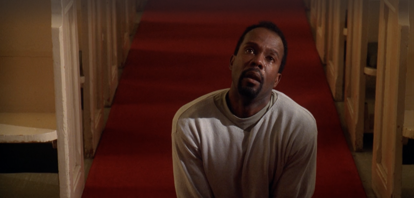 Pastor Barnes kneeling in the aisle of a church, looking up at the camera, with tears on his face.