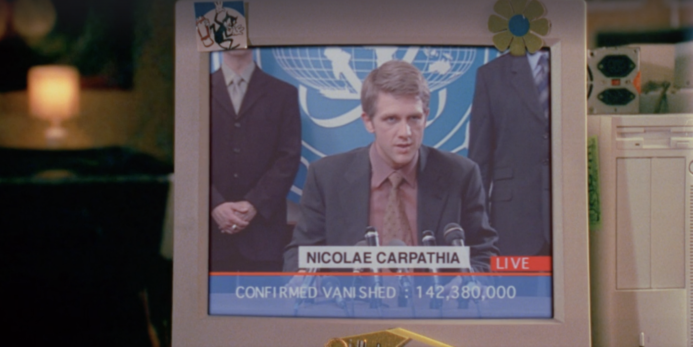 CRT computer screen showing a gaunt young-ish man with sunken eyes and perfectly in-place dirty blonde hair, wearing a grey blazer and reddish pink shirt and tie, at the lectern at a press conference. Behind him is a blue logo that seems to be inspired by the UN one. At the bottom of the screen is his name, "Nicolae Carpathia," plus a red box reading "LIVE" and a ticker reading "Confirmed vanished: 142,380,000."