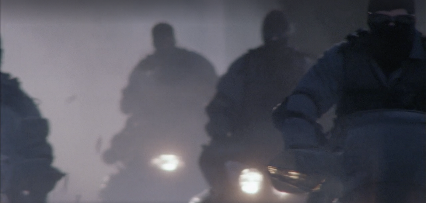 A gang of masked Skidoo riders with their lights on.