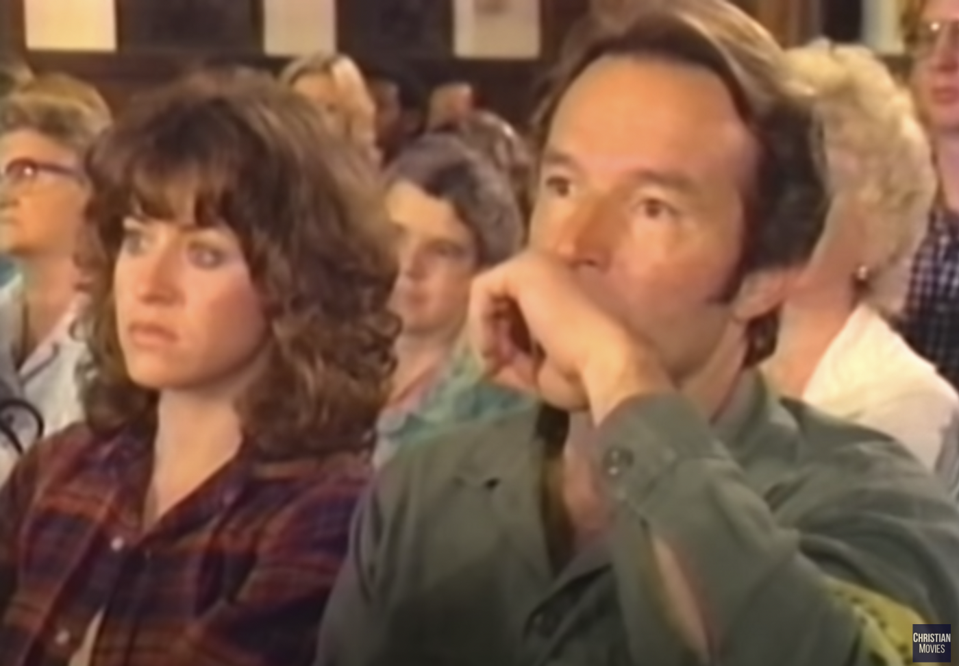 Kathy and David sitting in a pew in church. David is holding his hand to his mouth.