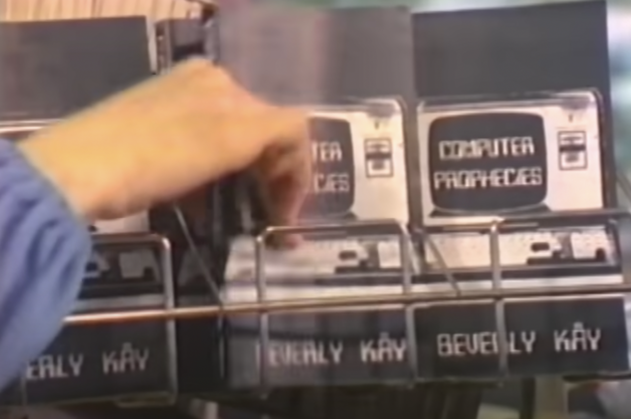 A hand reaching for a book entitled "Computer Propecies" by Beverly Kay, which has a picture of an era-appropriate computer on a display rack.