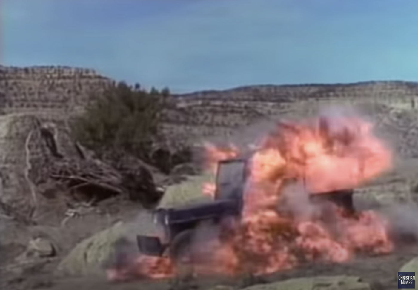 An old green open-top Jeep on fire in a Southwestern desert ladscape.