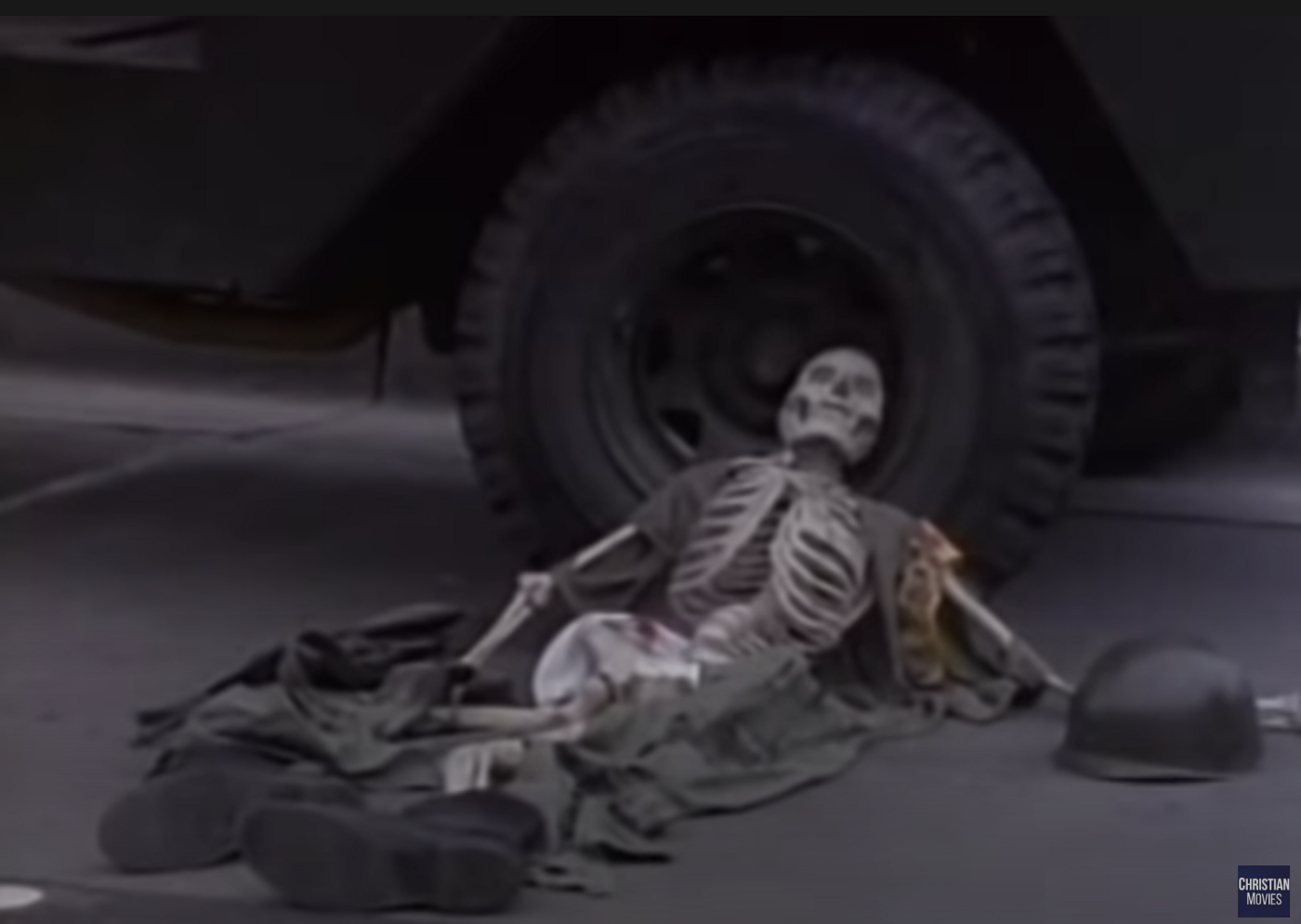 A skeleton wearing what's left of a Unite soldier's uniform. collapsed against the wheel of the RV (or a different, parked military RV?).