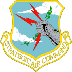 Crest with the text "Strategic Air Command" and an armoured fist holding three red lightning bolts and an olive branch, against a background of a blue sky and a few clouds.
