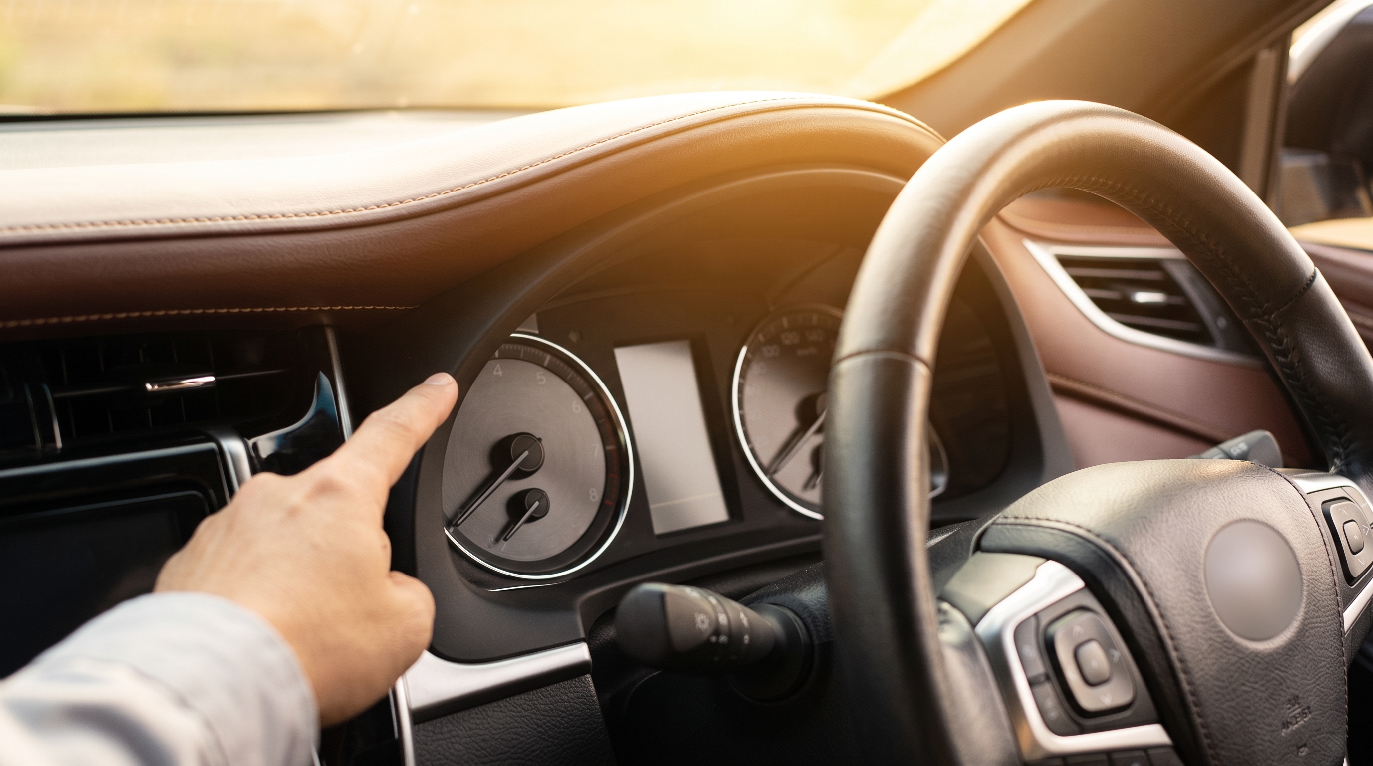 明るい日差しが差し込むSUVの車内で、運転席のメーターパネルを中心に捉えたクローズアップ写真。状態を確認する査定士の指先がわずかに写り込んだシーンです。